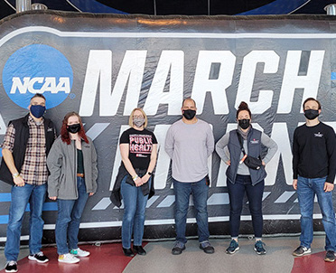 A team of researchers from Fairbanks School of Public Health and Regenstrief Institute stand in front of March Madness sign at the NCAA Men's Basketball Tournament.
