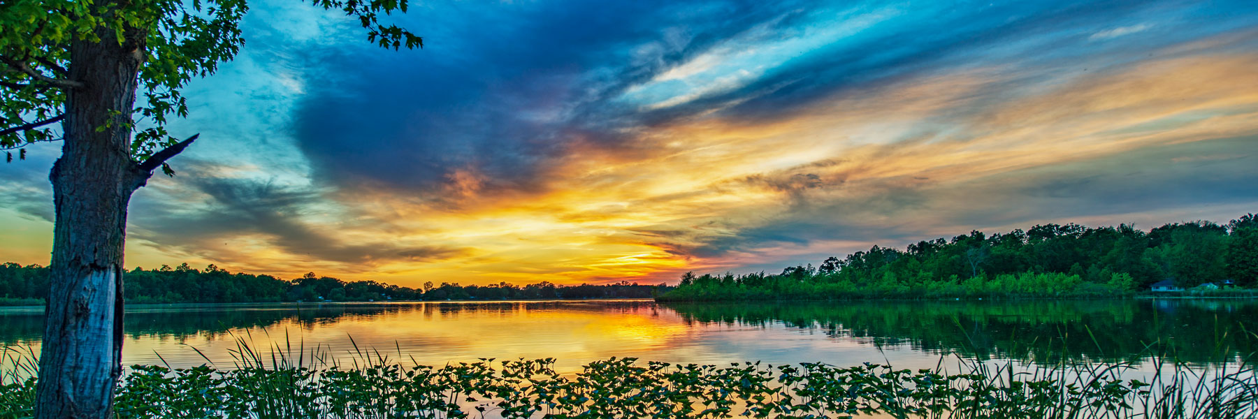 sunset over a lake with the sky showing contrasting colors of blue, yellow, orange and red