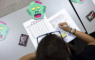 student completing zombie apocalypse exercise with pen and paper at desk