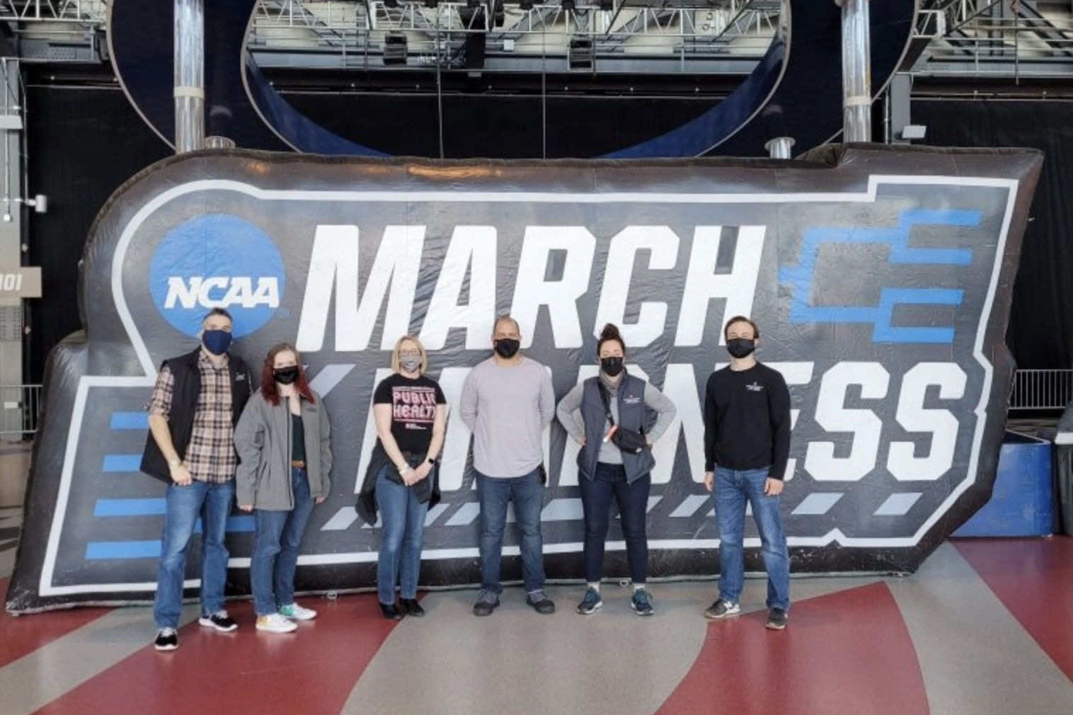 group of people wearing masks in front of march madness sign